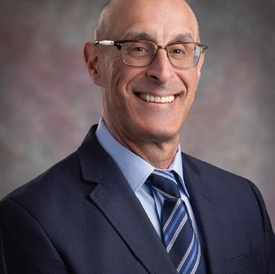 Smiling man in suit and glasses against a blurred background.