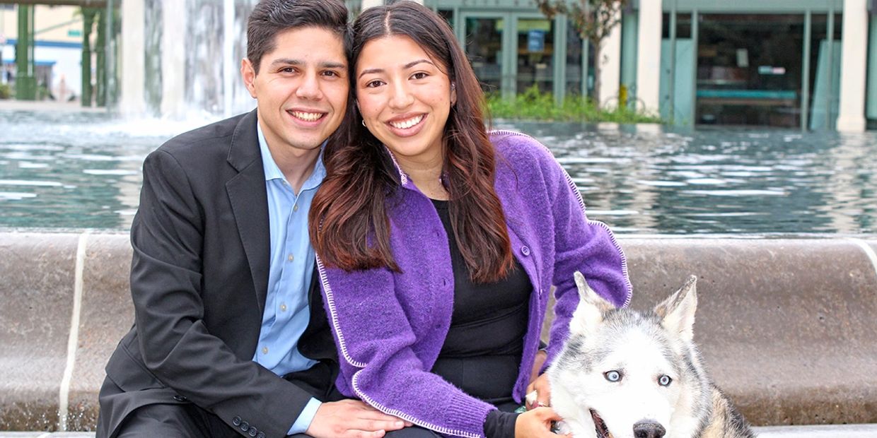 Happy couple sitting by a fountain with their husky dog.
