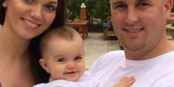 A happy family portrait with a mother, father, and baby smiling outdoors.