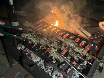 Kebabs grilling over hot coals on a barbecue at night.