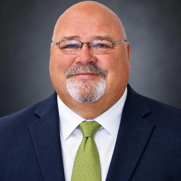 Smiling bald man with glasses and a beard in a suit and green tie.