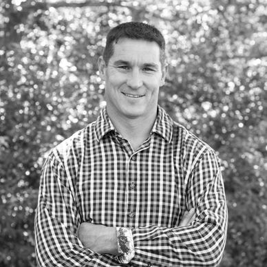 Smiling man with arms crossed, wearing checkered shirt outdoors.