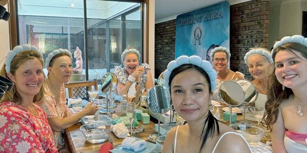 Photo from a actual Opulent Aura skincare party, many women gathered around a table, smiling.
