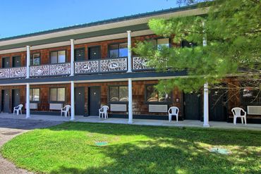 Two-story motel with brown siding and white plastic chairs outside rooms.