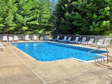 Outdoor swimming pool surrounded by white lounge chairs and lush green trees.