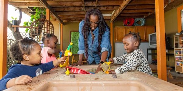 Woman engaging with three children in a playful learning activity at a wooden table.