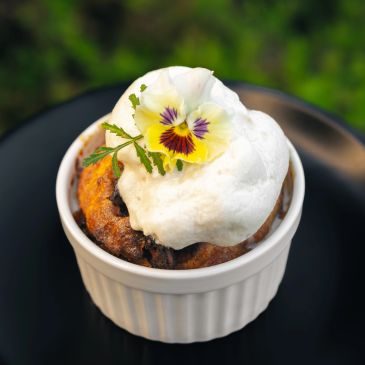 Ramekin dessert topped with cream and edible flower.