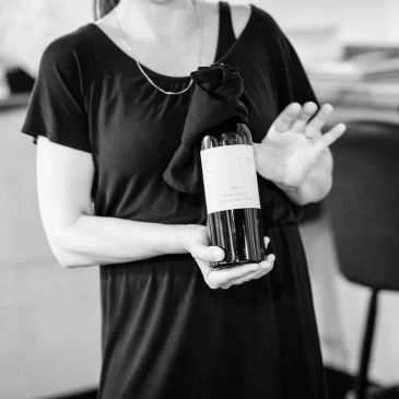 Person in black dress holding a wine bottle with a cloth.