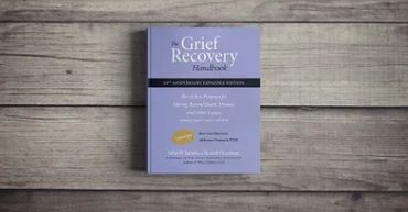 A copy of The Grief Recovery Handbook on a wooden surface.