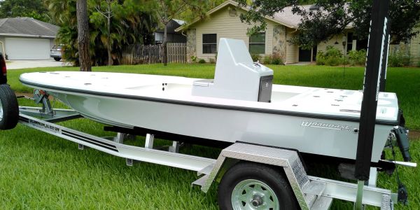White flat-bottomed boat on a trailer in a yard.