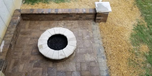 A circular fire pit on a paved patio with straw and grass surrounding it.