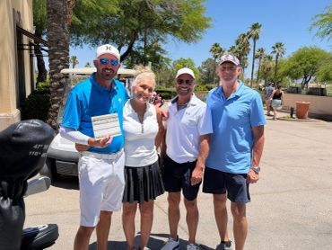Group of four golfers posing outdoors on a sunny day.