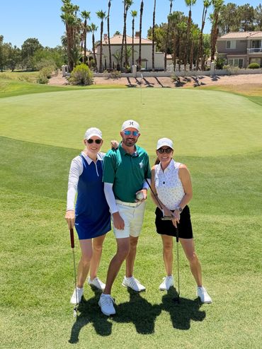 Three people posing on a golf course with clubs.
