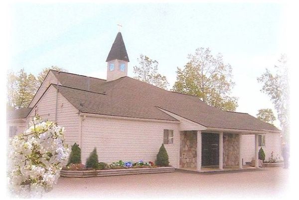 Small white church with steeple and flower beds.