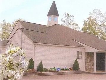 Small church building with a steeple and light exterior.