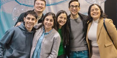 Group of six friends smiling together indoors.