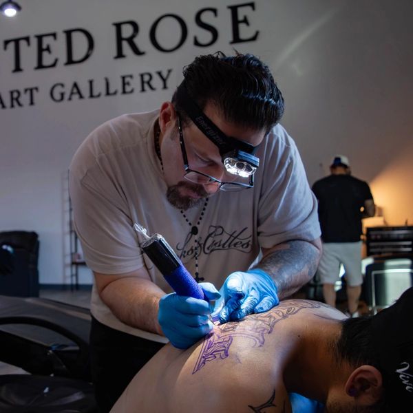 Tattoo artist focused on inking a detailed back tattoo in a studio.