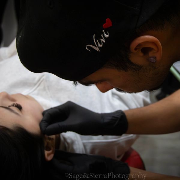 A tattoo artist carefully working on a client's face with precision.