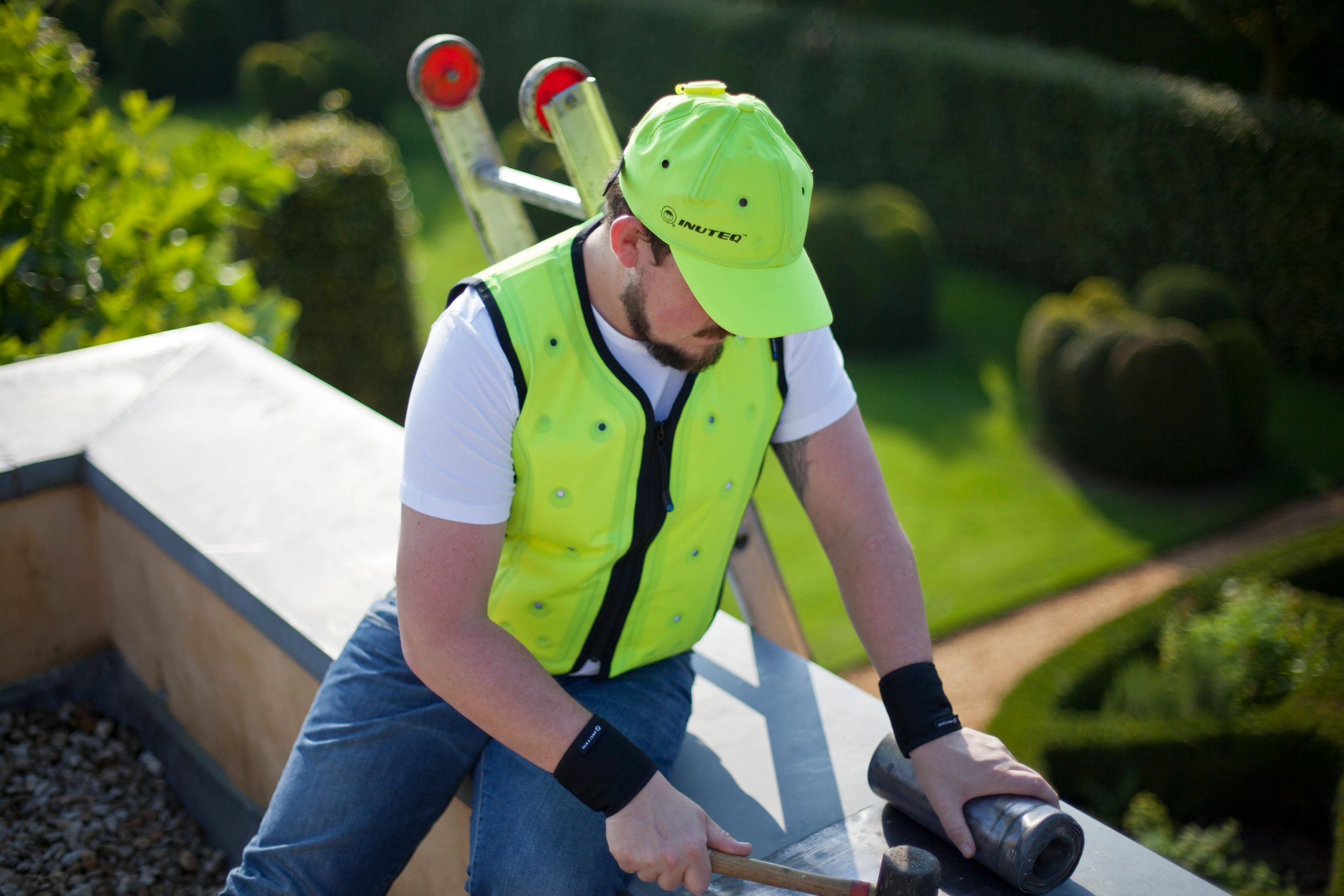 Man on rooftop works wearing Inuteq Bodycool Smart cooling vest in yellow and headcool smart cap