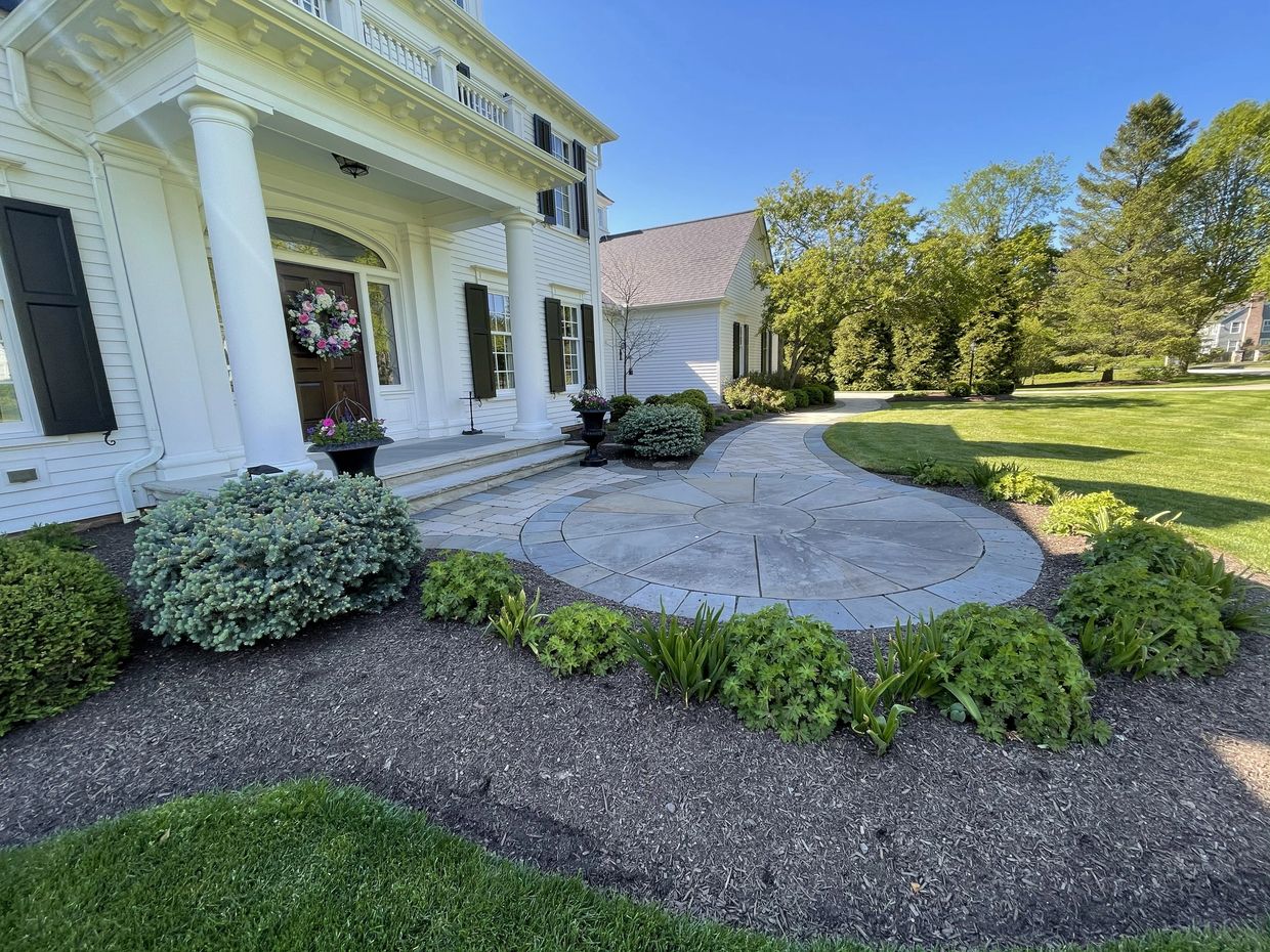Elegant white house with a curved stone pathway and lush landscaping.