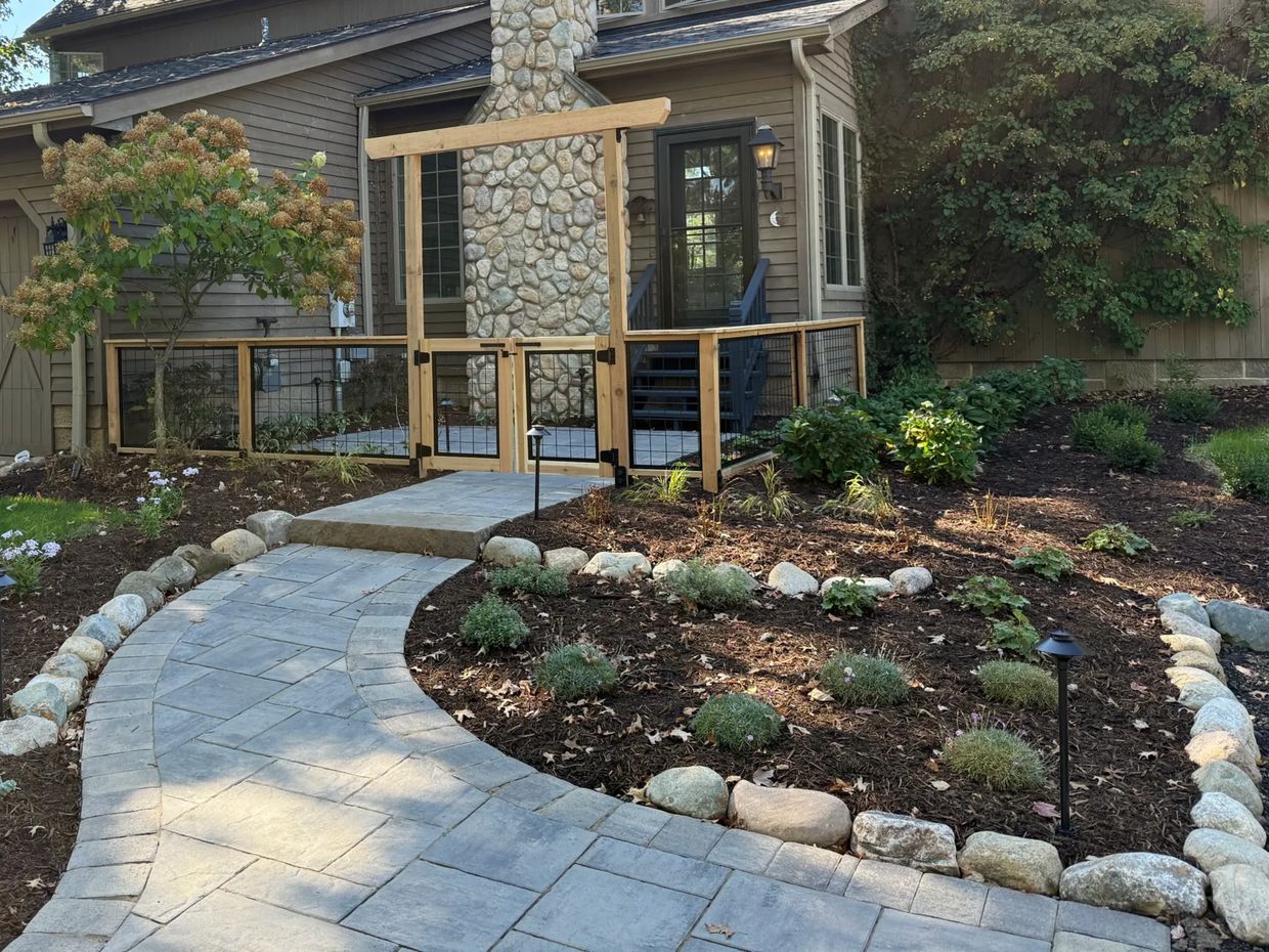 Stone pathway leads to a wooden gated porch with garden beds and landscaped plants.