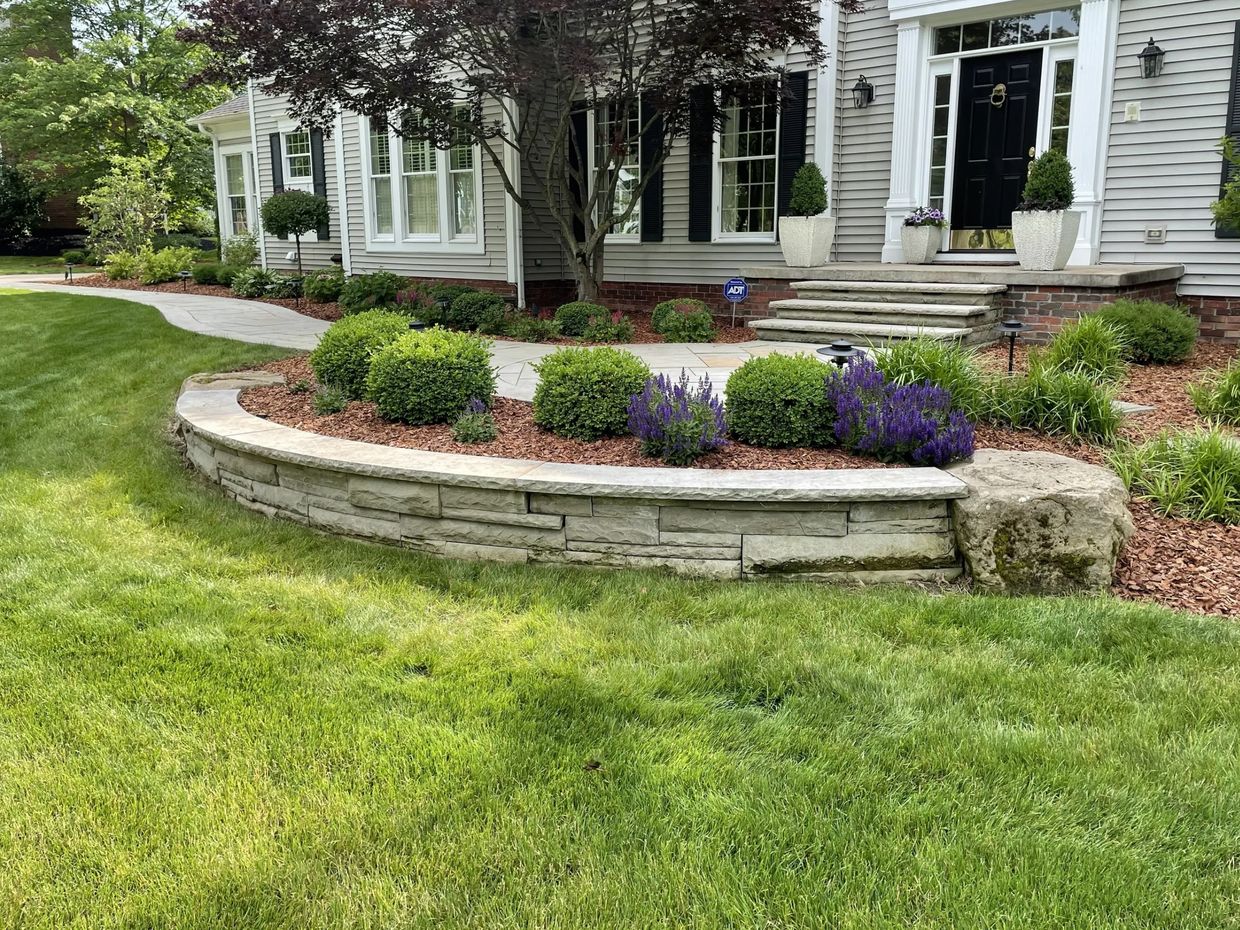 Neatly landscaped front yard with stone wall, green bushes, and purple flowers by a classic Broadview Heights Ohio house entrance.