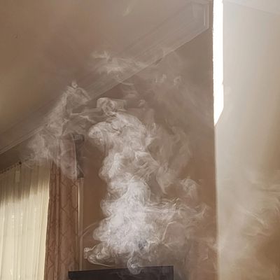 White smoke swirling inside a sunlit room near a window.