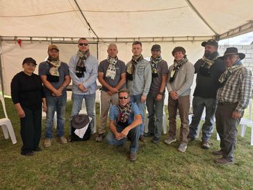Group of people posing together under a tent, most wearing scarves around their necks.