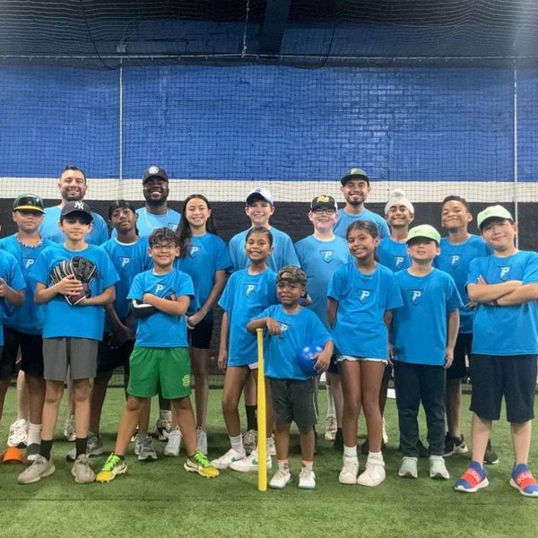 Youth baseball team and coaches posing indoors on turf field.