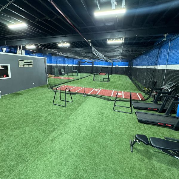 Indoor sports training area with artificial turf and agility hurdles.