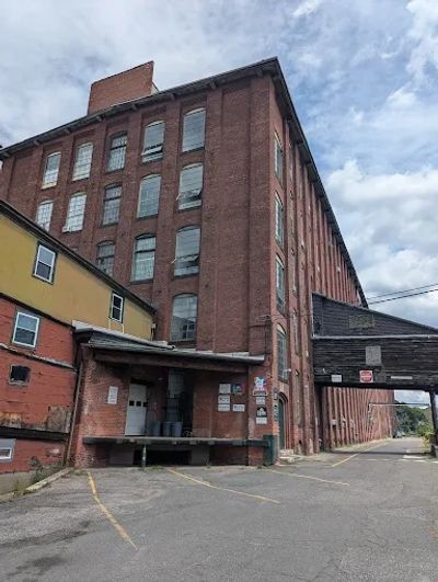 Old industrial brick building with multiple windows under a cloudy sky.