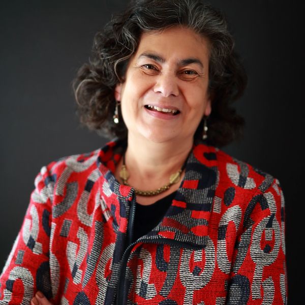 Woman with black and grey hair wearing red, grey and black jacket standing smiling