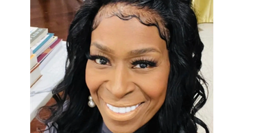 Smiling woman with styled black hair and pearl earrings.