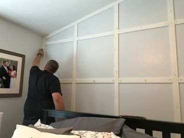Man installing decorative wall paneling in a bedroom.