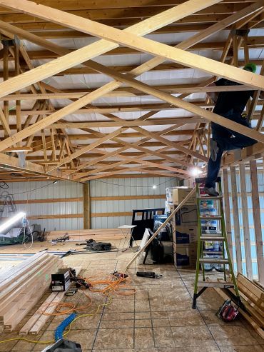 A worker on a ladder installing wooden trusses in a building under construction.