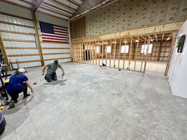 Two people working on a large concrete floor inside a warehouse with an American flag on the wall.
