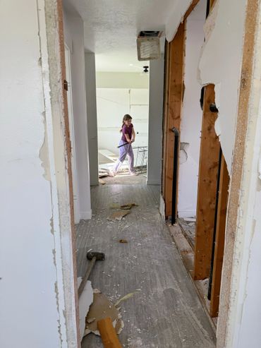 A hallway under renovation with exposed studs and a person walking in the background.