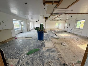 An empty, partially demolished room with exposed flooring and a trash bin.