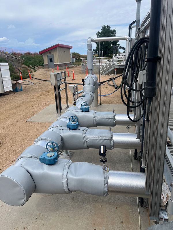 Insulated industrial pipes with blue valves and connected cables outdoors.