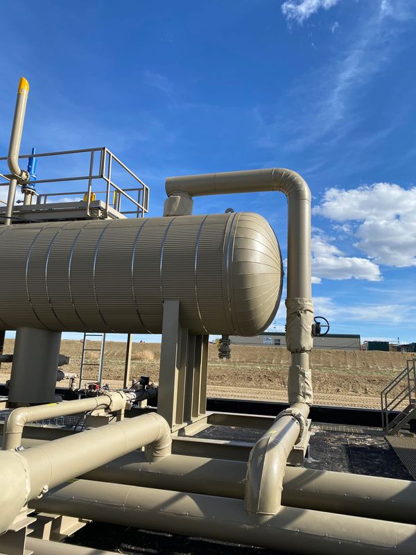 Industrial pipes and a large cylindrical tank under a blue sky.