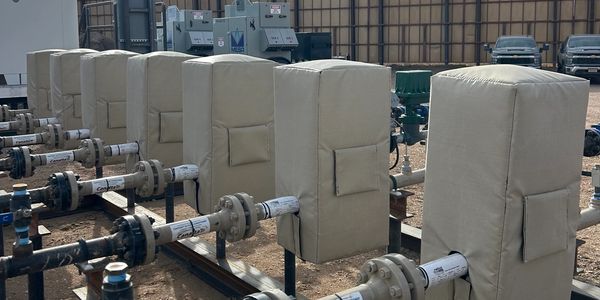 Insulated industrial pipes and equipment outdoors in an industrial area.