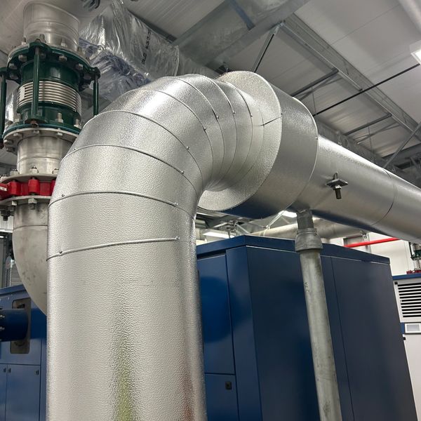 Large insulated industrial pipe bends in a mechanical room.