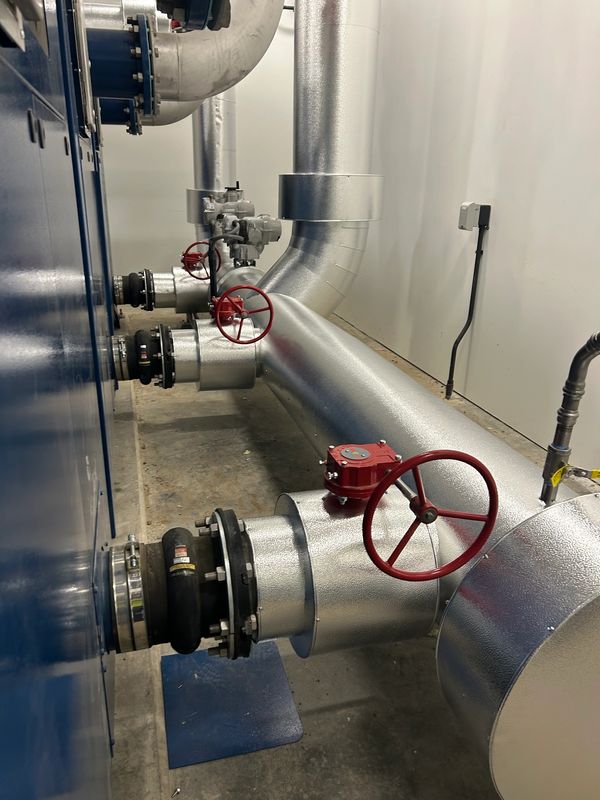 Industrial silver pipes with red valve handles inside a utility room.