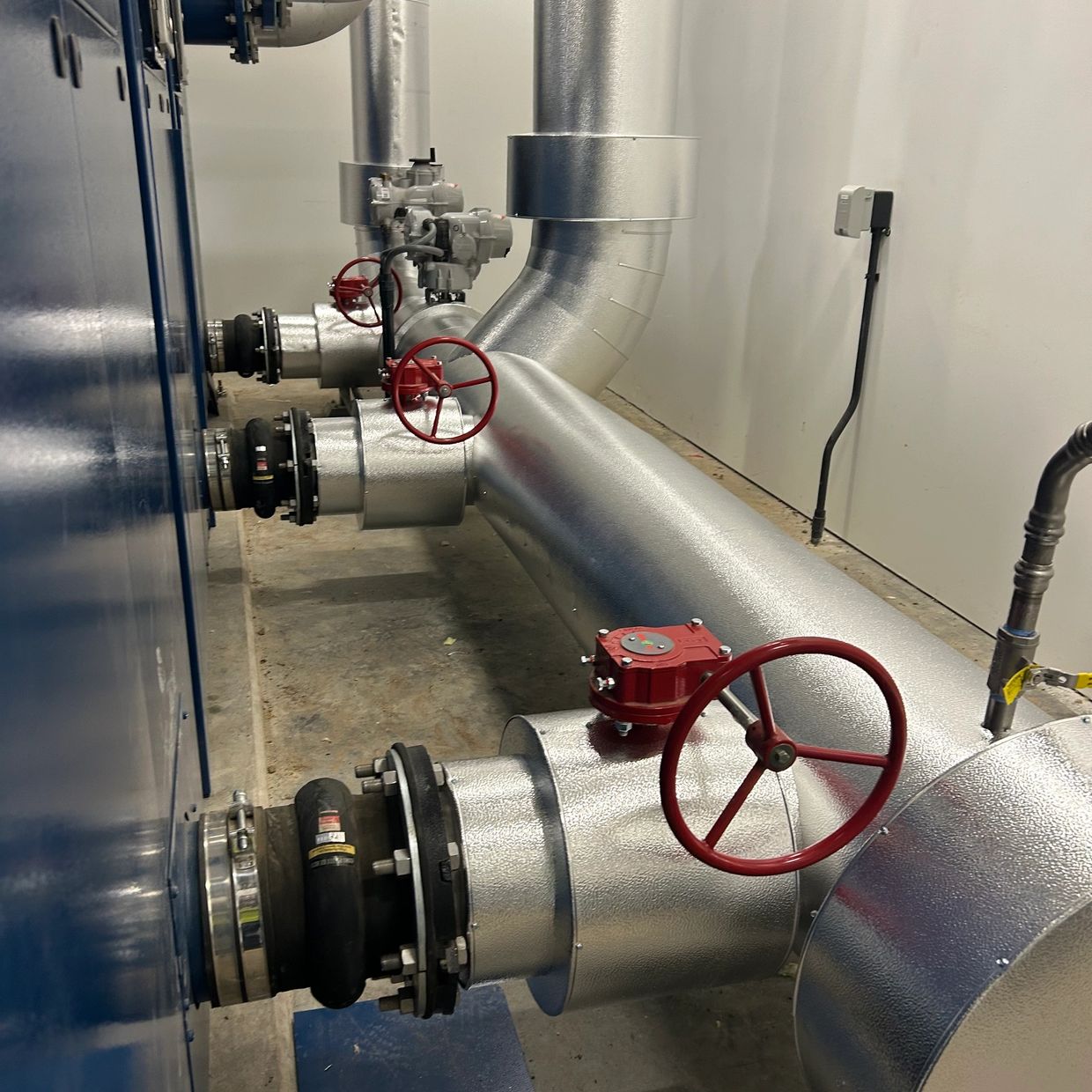 Industrial pipes with red valve wheels in a utility room.