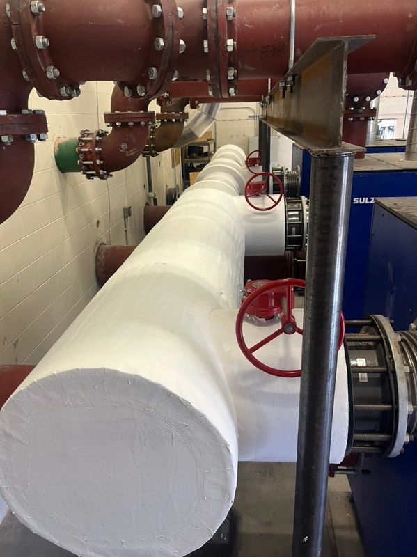 Insulated white pipes with red valve wheels in an industrial setting.