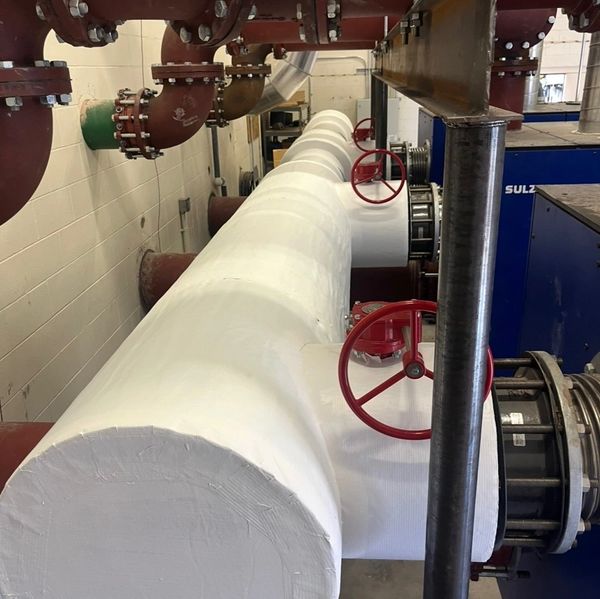 Large industrial insulated pipes with red valve wheels in a utility room.