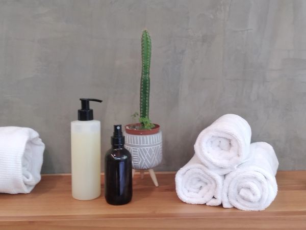Stacked white towels, lotion and spray bottles, and a cactus on a wooden surface.