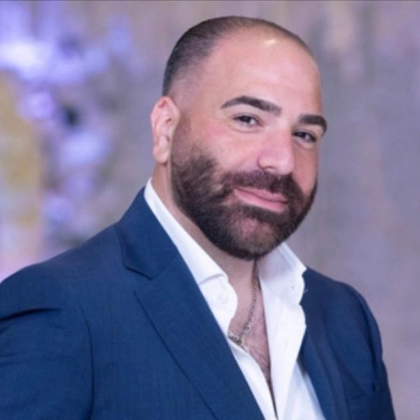 A confident man in a blue suit and white shirt smiling.