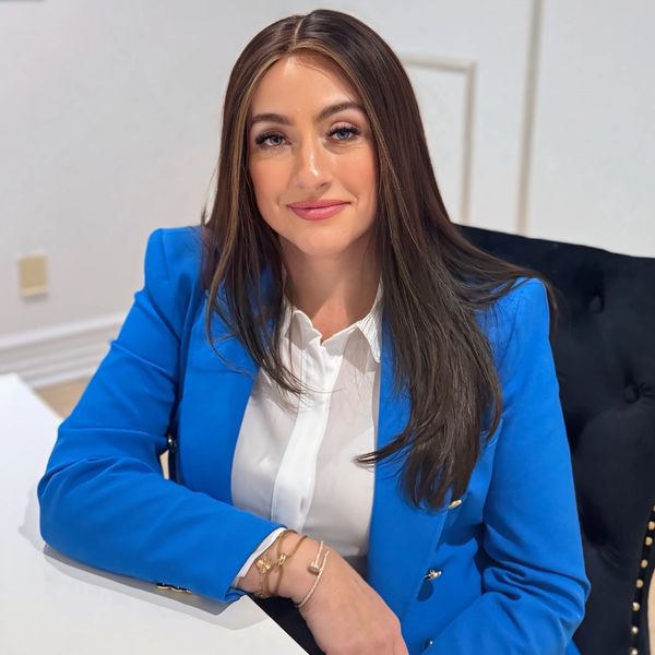 Woman in a blue blazer sitting at a white table, smiling.