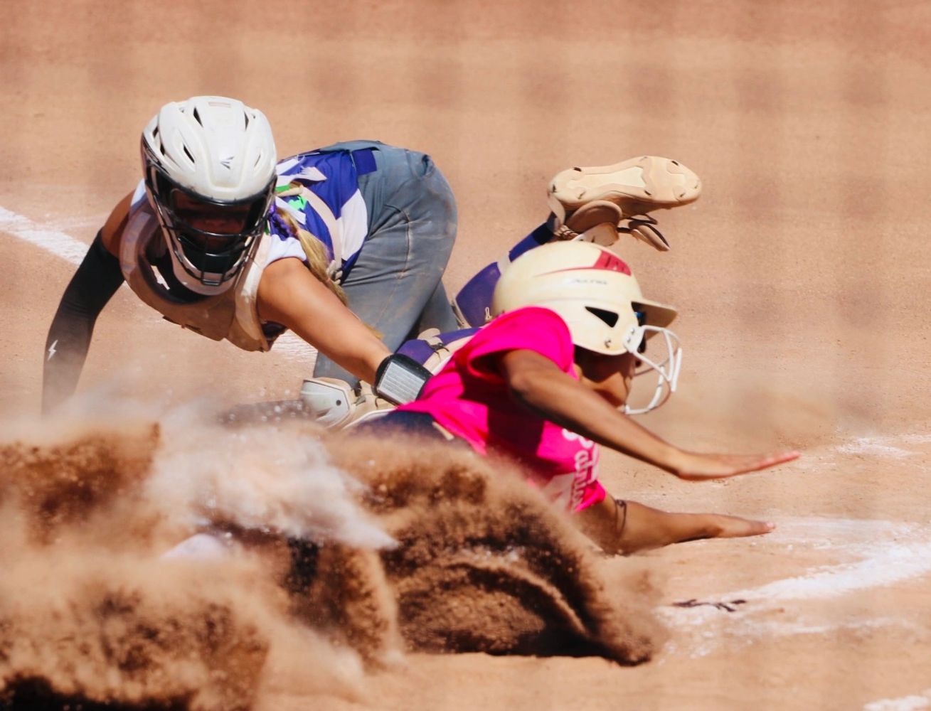 A softball player slides into home plate as the catcher attempts to tag her out.